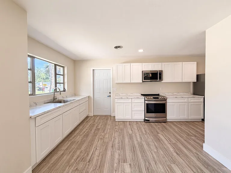 Spacious kitchen with ample white cabinetry, stone-look counters, large window over sink, and stainless range & microwave.