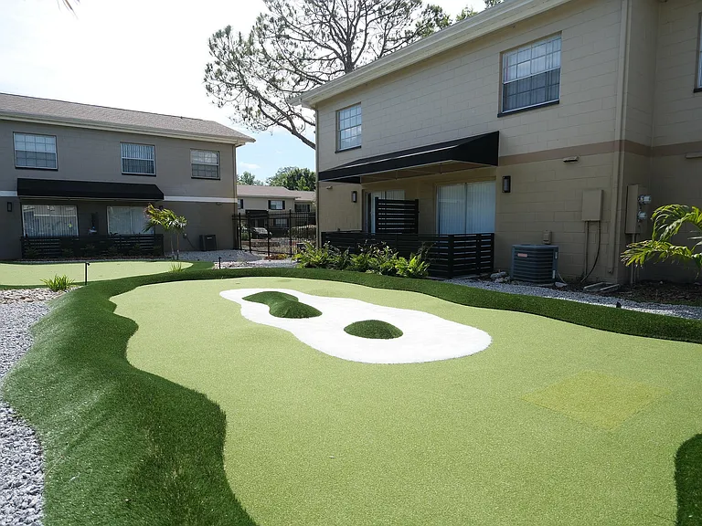 Charming apartment complex with a beautifully landscaped mini-golf area surrounded by cozy, well-maintained two-story buildings.