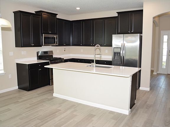 Kitchen has staggered cabinet design, stainless steel appliances, quartz countertops, recessed lighting.
