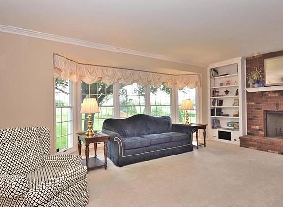 Large great room boasts triple bay window for lots of natural light, crown molding and floor-ceiling brick wood-burning fireplace flanked by elegant bookshelves.