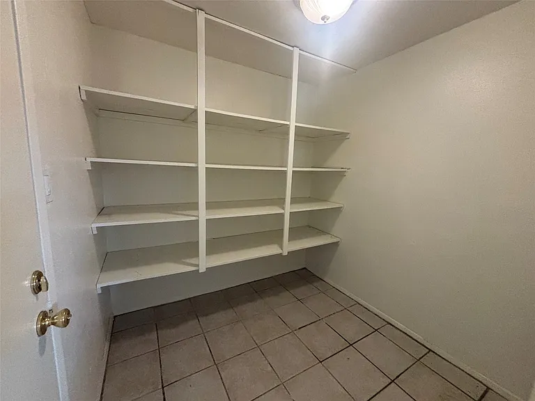 Walk-in pantry featuring multiple white shelving units and tile flooring