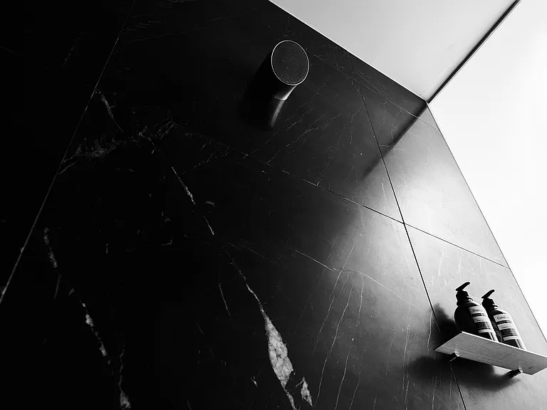 Sculptural Shower with Dramatic Stone Finishes _ This striking shower design features bold veined black stone, precision-cut paneling, and integrated shelving.