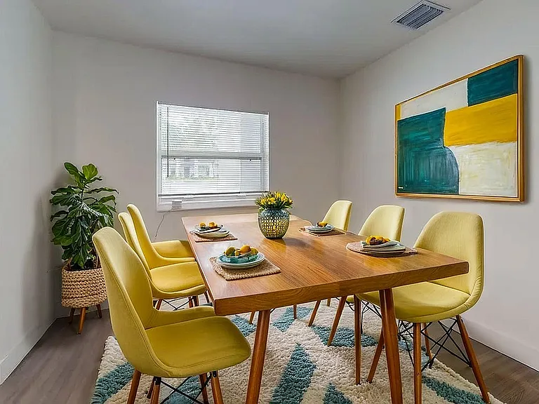 Bright and inviting dining room with modern wooden table, cheerful yellow chairs, vibrant artwork, and fresh decorations.