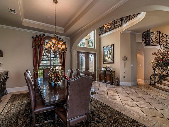 The elegant formal dining room has a grand bronze-finish chandelier hanging from a tray ceiling with crown molding in and out. An arched window offers custom plantation shutters and views of the front yard landscaping.