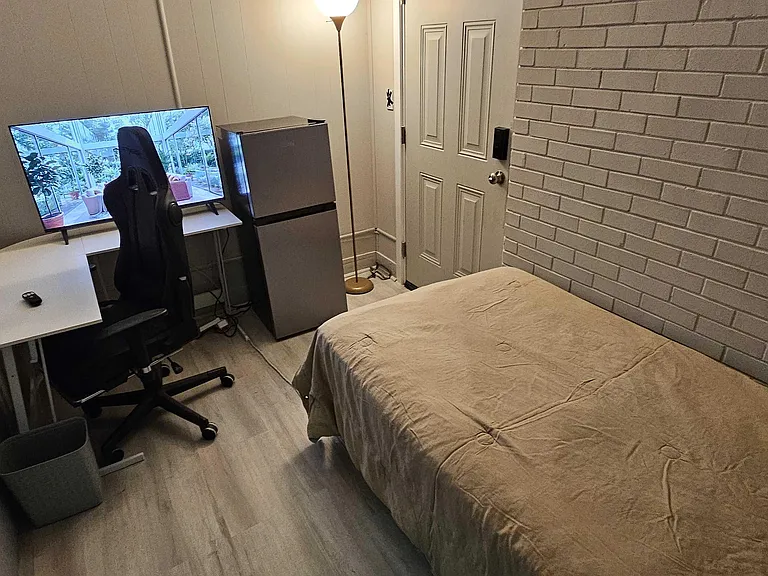 Furnished bedroom with a bed, dedicated desk/work area, and compact mini fridge for added convenience.
