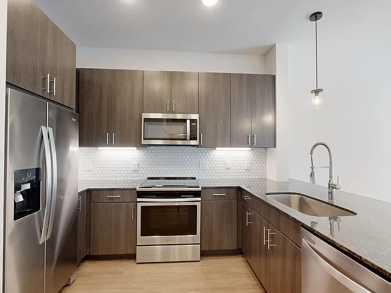 Apartment kitchen with stainless steel appliances, granite countertops, and wood-style flooring.