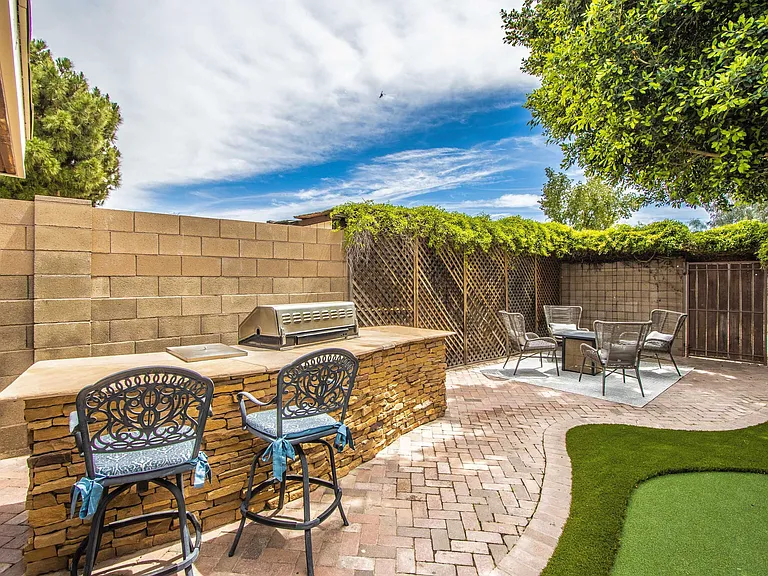 Outdoor oasis at Casa Del Sol, Tempe rental home. Features a built-in stone BBQ island, bar seating, brick pavers, a putting green, and a separate patio chat set with a fire pit table. Perfect backyard for a top Tempe, AZ vacation stay
