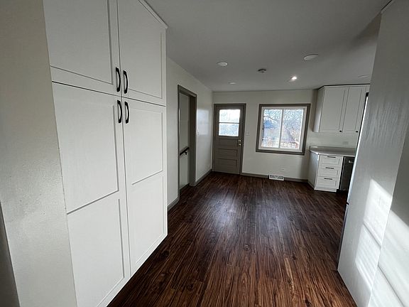 Walking from entryway toward kitchen. Large storage cupboards to the left. The grey door opens onto back deck. Doorway in left corner goes down 3 steps to family room/bonus room.