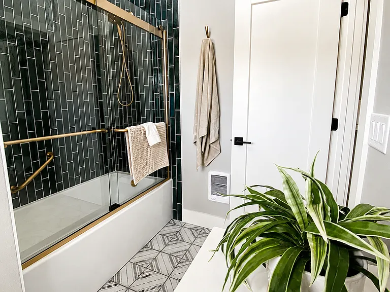 Bathroom features extra deep tub, champagne bronze fixtures, rich green/blue tiles, handheld option for shower, and grab bars. Extra Large "Towel Sheets," hand towels, and wash cloths, and bath mat provided.