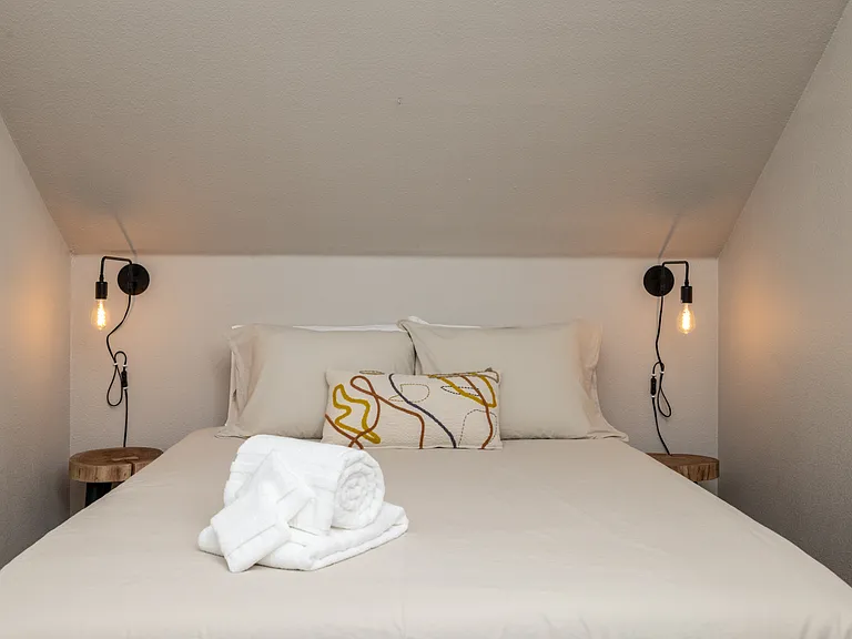 Charming fifth bedroom with a queen bed, cozy sloped ceiling, and warm hanging lights on each side_perfect for a restful, intimate vibe. This bedroom is located upstairs.