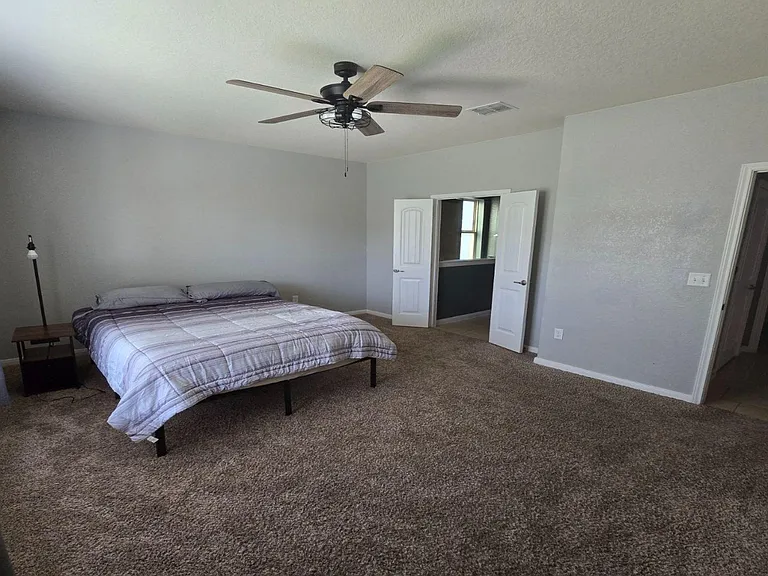 Spacious carpeted bedroom with ceiling fan, large window with drapes, and convenient access to closet and bath.