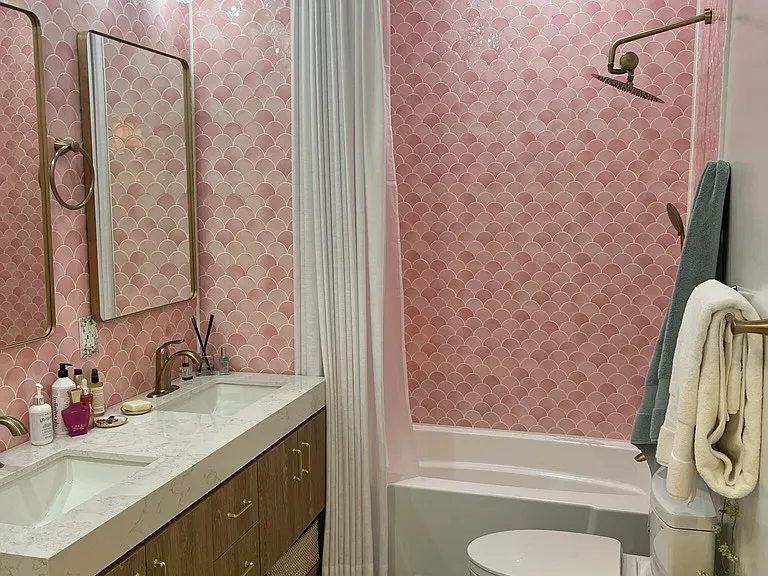 A double-sink vanity, brass fixtures, playful pink tile, and a skylight that fills the space with beautiful natural light.