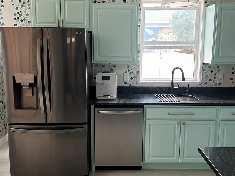 Cheerful, light-filled kitchen with mint cabinetry, stainless-steel appliances, dramatic botanical wallpaper, generous storage, and a deep sink beneath the window.