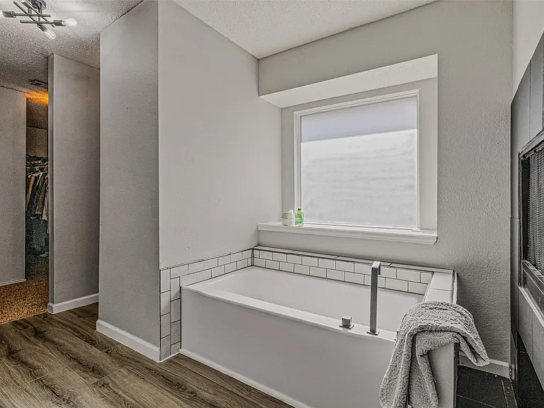 Built-in soaking tub with subway tile surround and wood-finish flooring