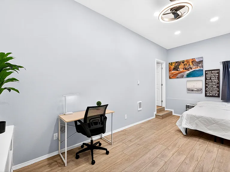 Spacious bedroom featuring wood-look flooring, a comfortable bed, and a dedicated desk area for work or study.