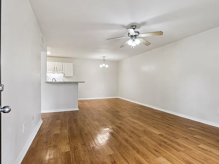 Bright and inviting open-plan living area with wood-style flooring and modern ceiling fans, adjacent to a compact kitchen featuring sleek cabinetry. Bright and inviting open-plan living area with wood-style flooring and modern ceiling fans, adjacent to a 