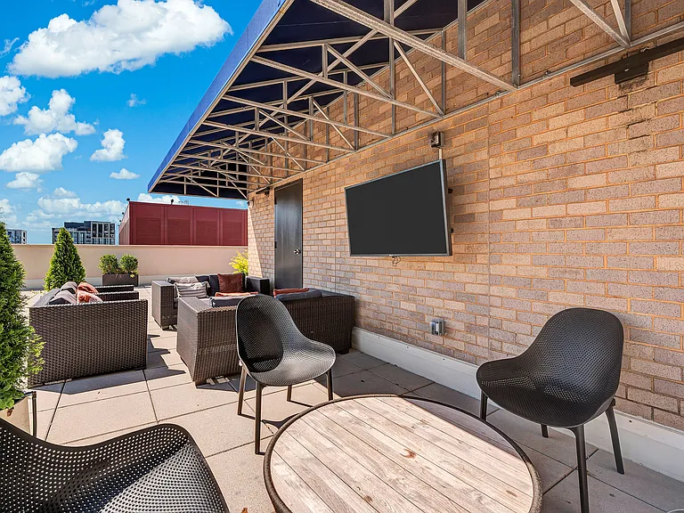 A patio with a table, chairs and a television on a brick wall.
