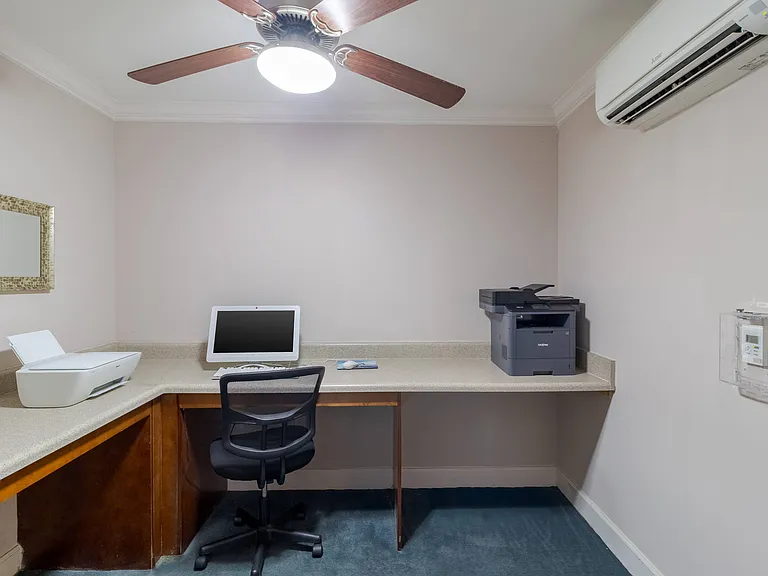 Private business center at Snowden Senior Apartments featuring desktop computer, multi-function printers, ample counter space, and ergonomic chair.