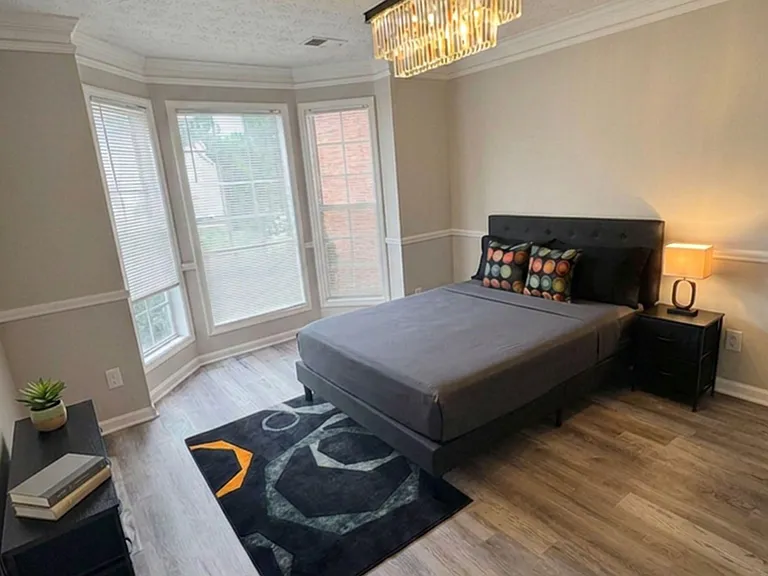 Spacious bedroom with a large bay window, wood-look flooring, and space for a nightstand and additional seating.