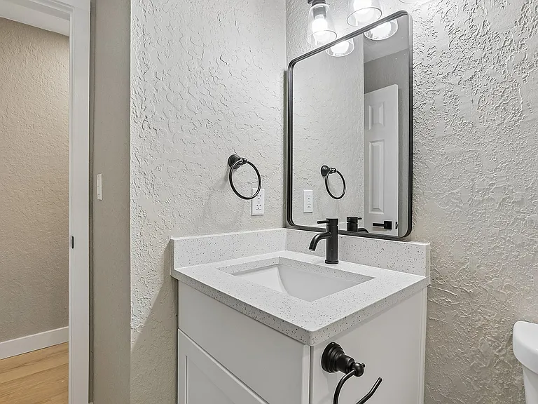 Modern bathroom with elegant black fixtures, a large mirror, and a sleek white vanity with textured walls.