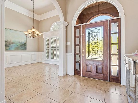 Tiled entrance foyer with a healthy amount of sunlight, crown molding, decorative columns, and an inviting chandelier