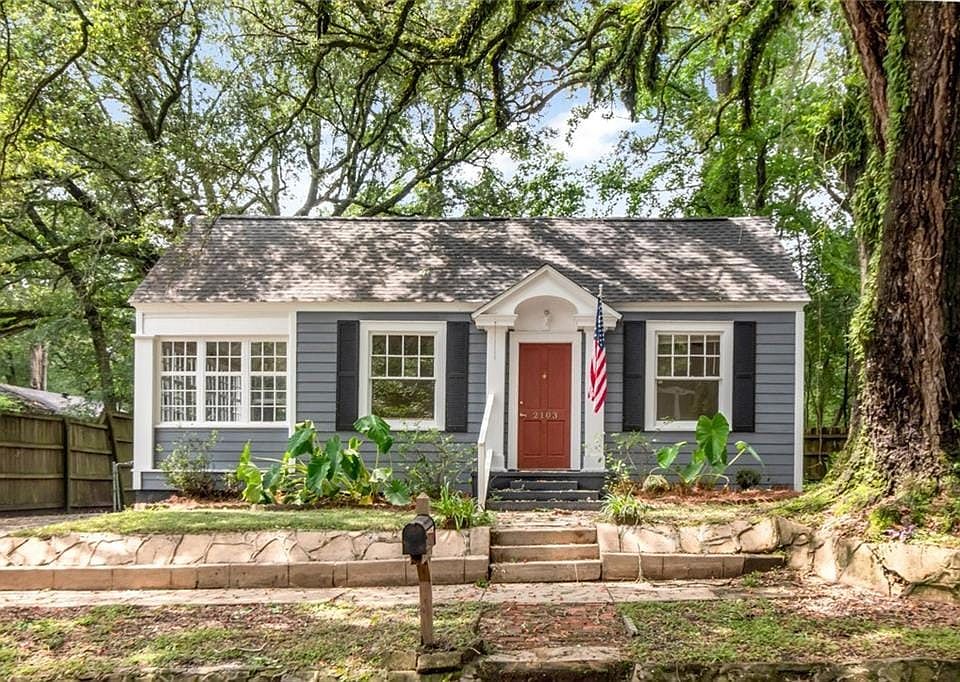 Charming cottage exterior with gray siding, white trim, and a red entry door