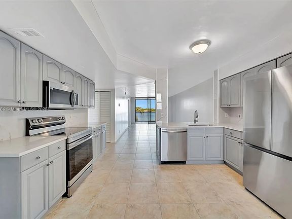 Kitchen as viewed from front door. Also seen is the entire length of the living area, the balcony, and unimpeded lake view. Kitchen has new quartz countertops, backsplash, fixtures and appliances.