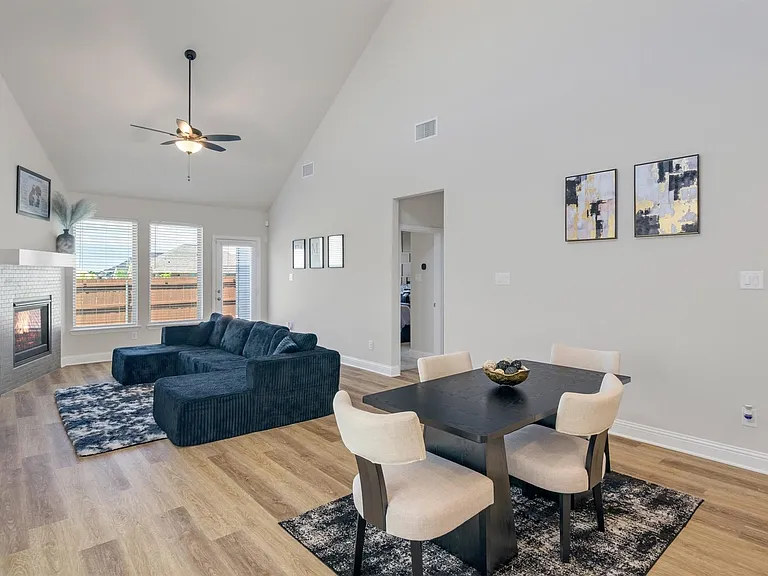 Vaulted ceilings enhance this open concept living space featuring wood-finish flooring, a contemporary fireplace with a tiled surround, and multiple windows
