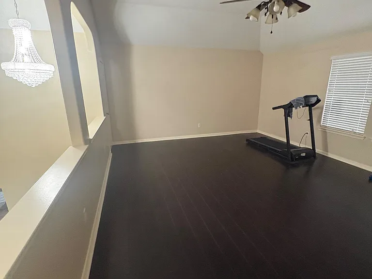 Spacious open living area with high ceilings, ceiling fan, and a large window with blinds; ideal for a flexible setup.
