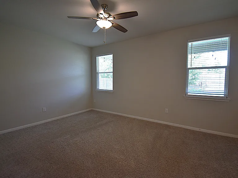 Primary bedroom features a ceiling fan and two large windows that provide plenty of natural light