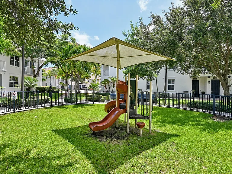 Vibrant playground with slide, surrounded by lush greenery and shade structures.