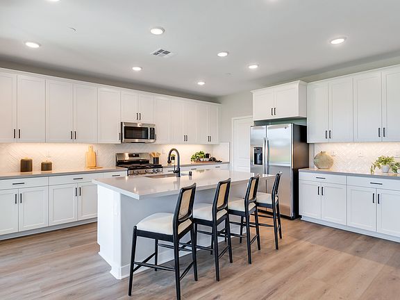 A modern, well-lit kitchen with white cabinets, a center island, and hardwood floors.