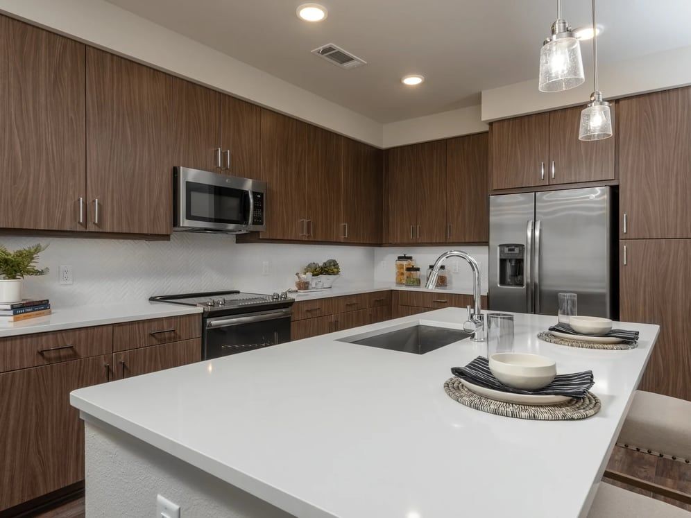 Finish Package I kitchen with white quartz countertops, dark cabinetry, white tile backsplash, stainless steel appliances, and hard surface flooring
