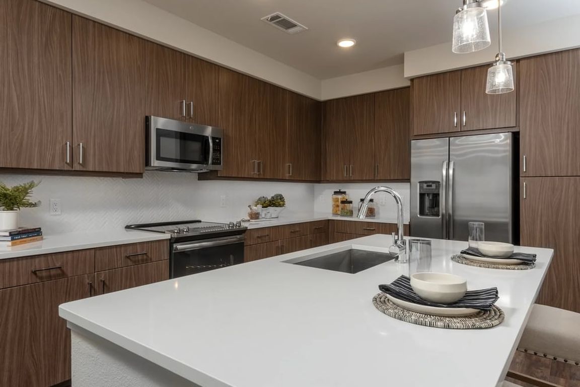 Finish Package I kitchen with white quartz countertops, dark cabinetry, white tile backsplash, stainless steel appliances, and hard surface flooring