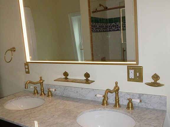 marble vanity with brass fixtures and lighted mirror