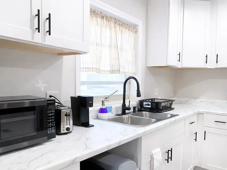 Updated kitchen with ample white cabinetry, marble-look counters, and a double-basin sink set beneath a window.