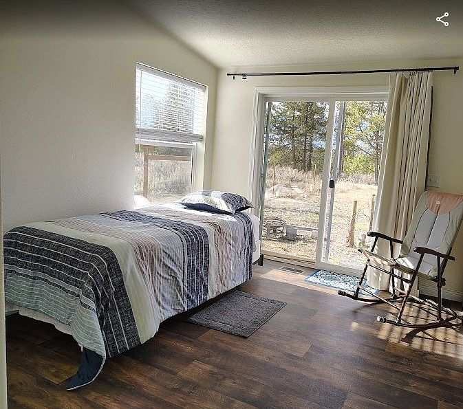 Large bedroom with plenty of natural lighting, private entrance and a spacious closet, dresser, rocking chair and extra long twin bed.