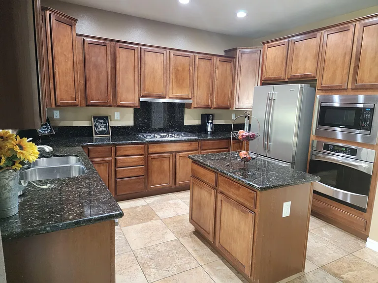 Spacious kitchen with ample wood cabinetry, granite counters, center island, and stainless-steel appliances.