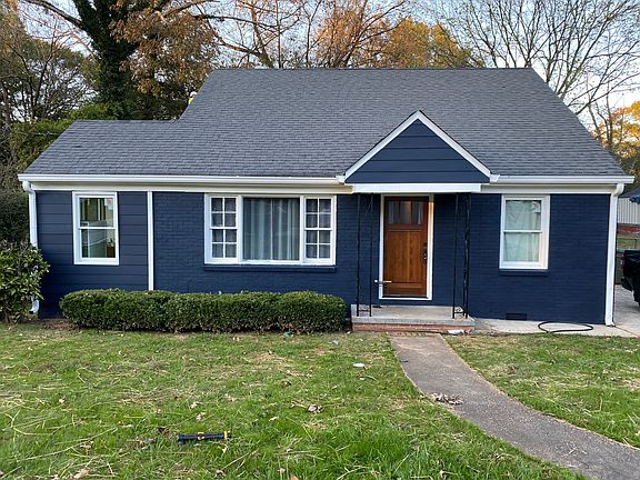 Charming navy blue bungalow with white trim, natural wood door, and covered entry. Large front windows, tidy shrubs, and a curved walkway add curb appeal. Nestled on a quiet street with mature trees, this home offers comfort and character.