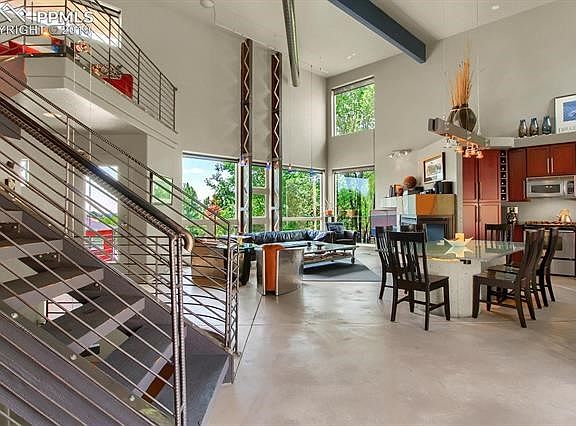Reverse view of the main level shows loft stairs in foreground, front door at back left, expansive windows and two I-beams that have been cut in a zig-zag pattern and reassembled for structural rigidity.