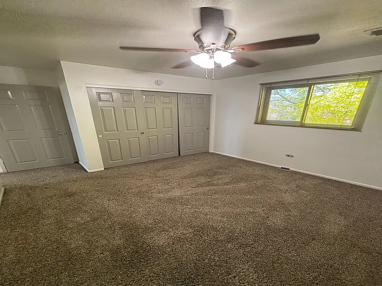 Bright bedroom featuring plush carpet, ample closet space, and a ceiling fan for comfort.