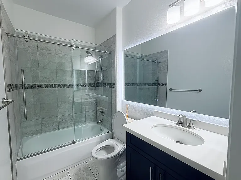 Upgraded guest bathroom featuring glass shower doors and back-lit heated mirror