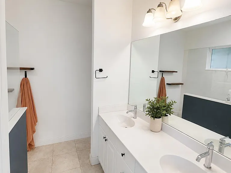 Clean bathroom with long double-sink vanity, ample counter space, large mirror, and tiled floor near the tub/shower.