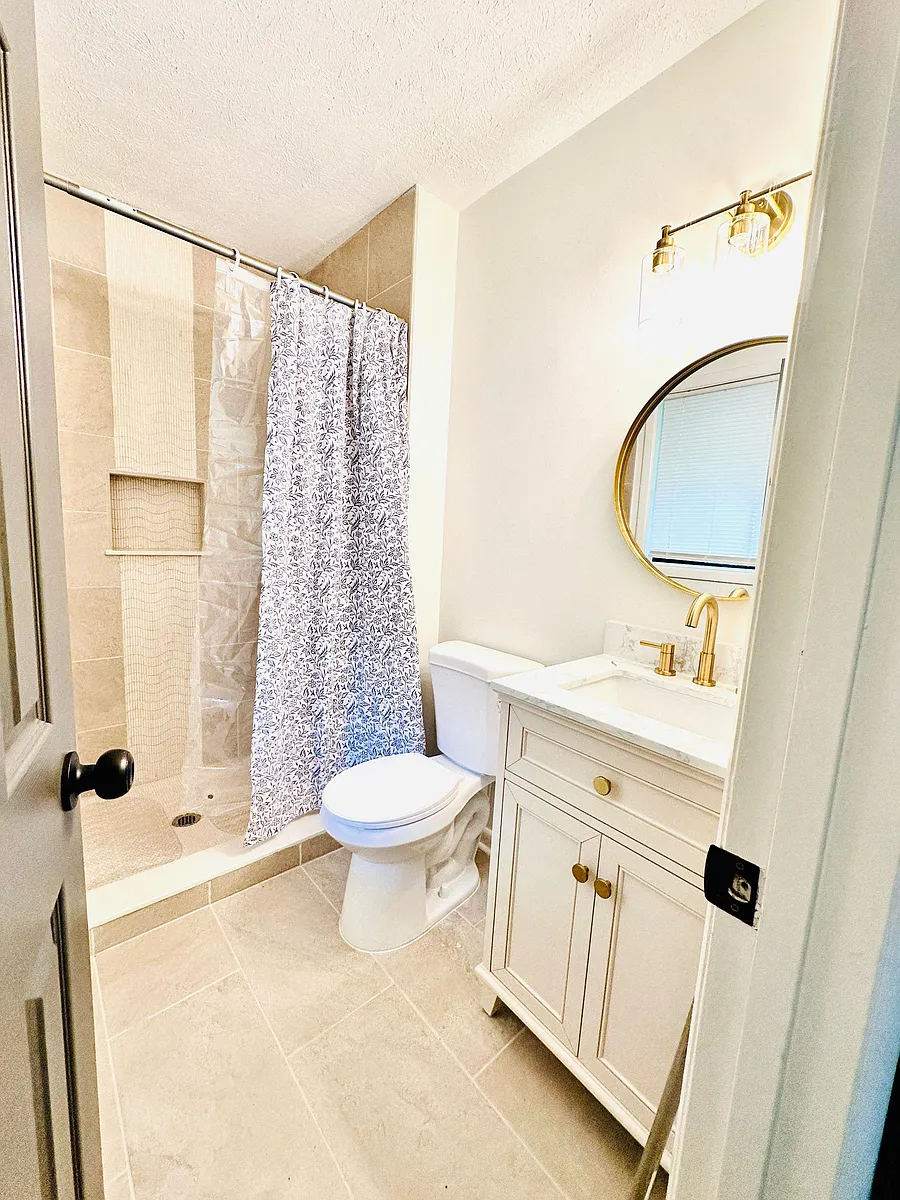 Updated bath with tiled tub/shower, vanity storage, and a contemporary round mirror with modern lighting. - Mercer Rd