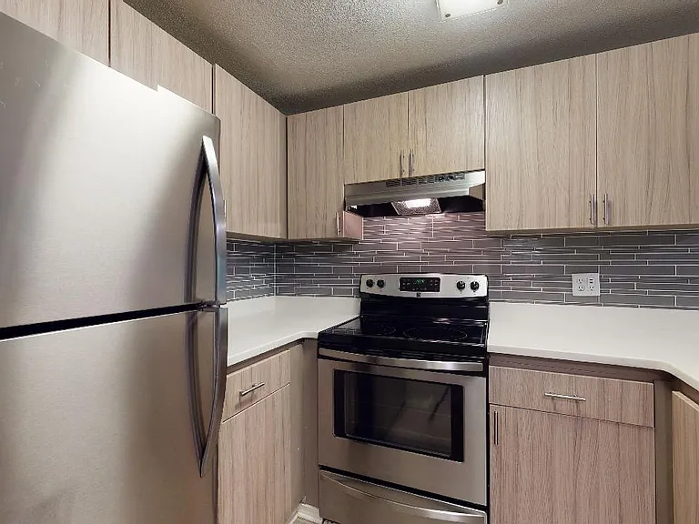 Apartment kitchen with stainless steel appliances, quartz countertops and wood-style flooring.
