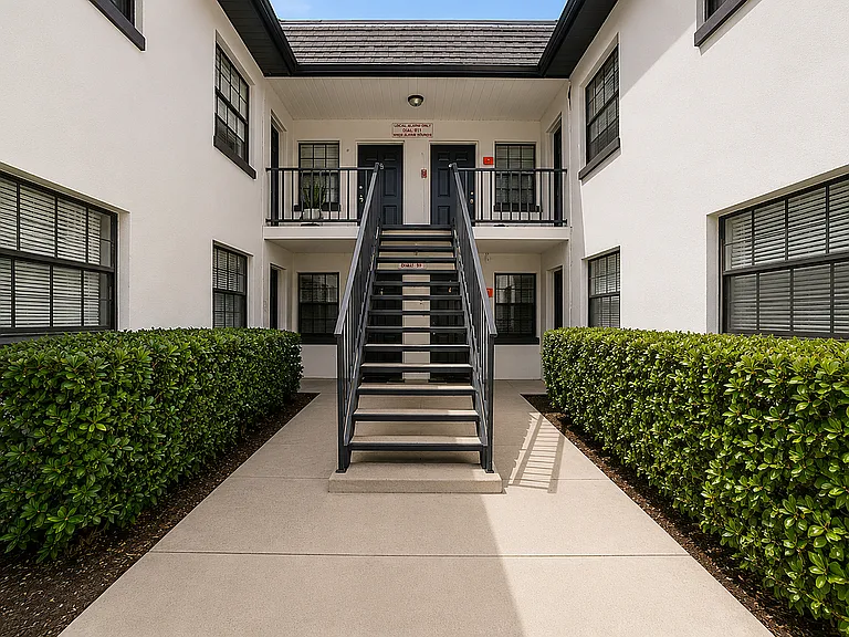 Charming apartment entrance with lush greenery, modern black railing, and stylish facade.