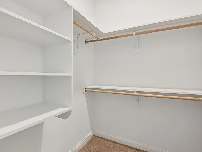 This spacious walk-in closet features built-in shelving and wooden hanging rods to provide a sophisticated and highly organized storage solution.