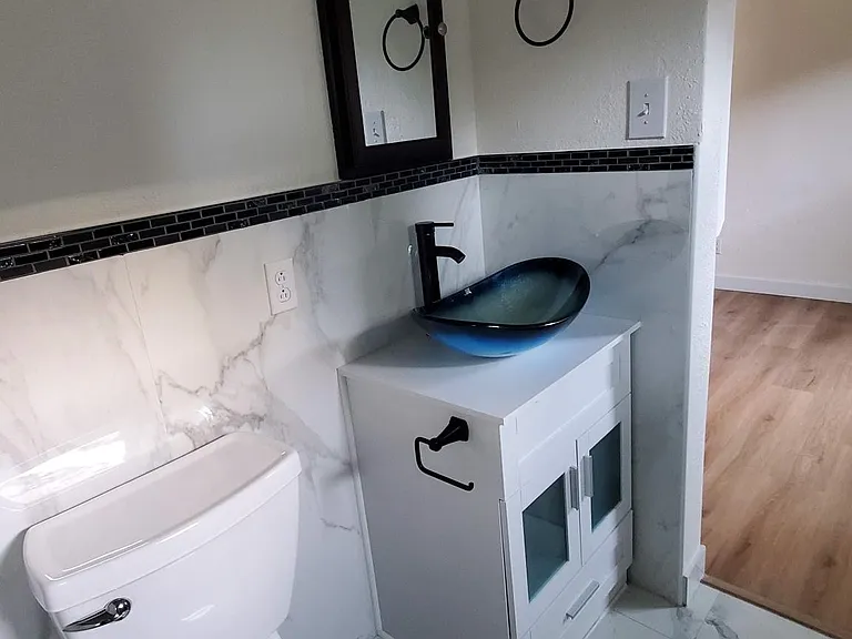 Bath glass sink, toilet and vanity and marble-like tile.