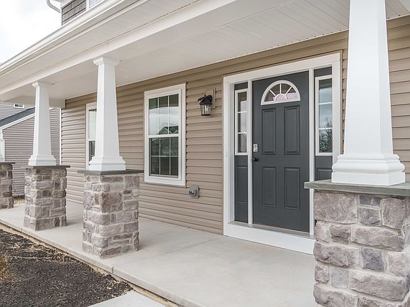 Covered front porch with stone column bases, white pillars, and a gray front door featuring glass si