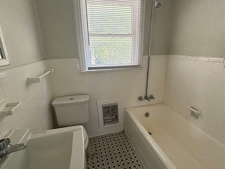 Bathroom featuring a window with blinds, a built-in bathtub with shower fixture, a toilet, and a sink